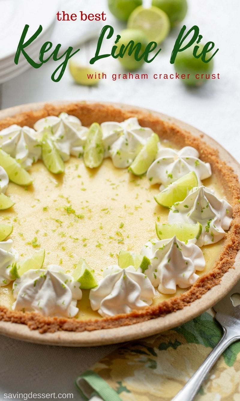 A creamy key lime pie decorated with whipped cream and limes in a graham cracker crust
