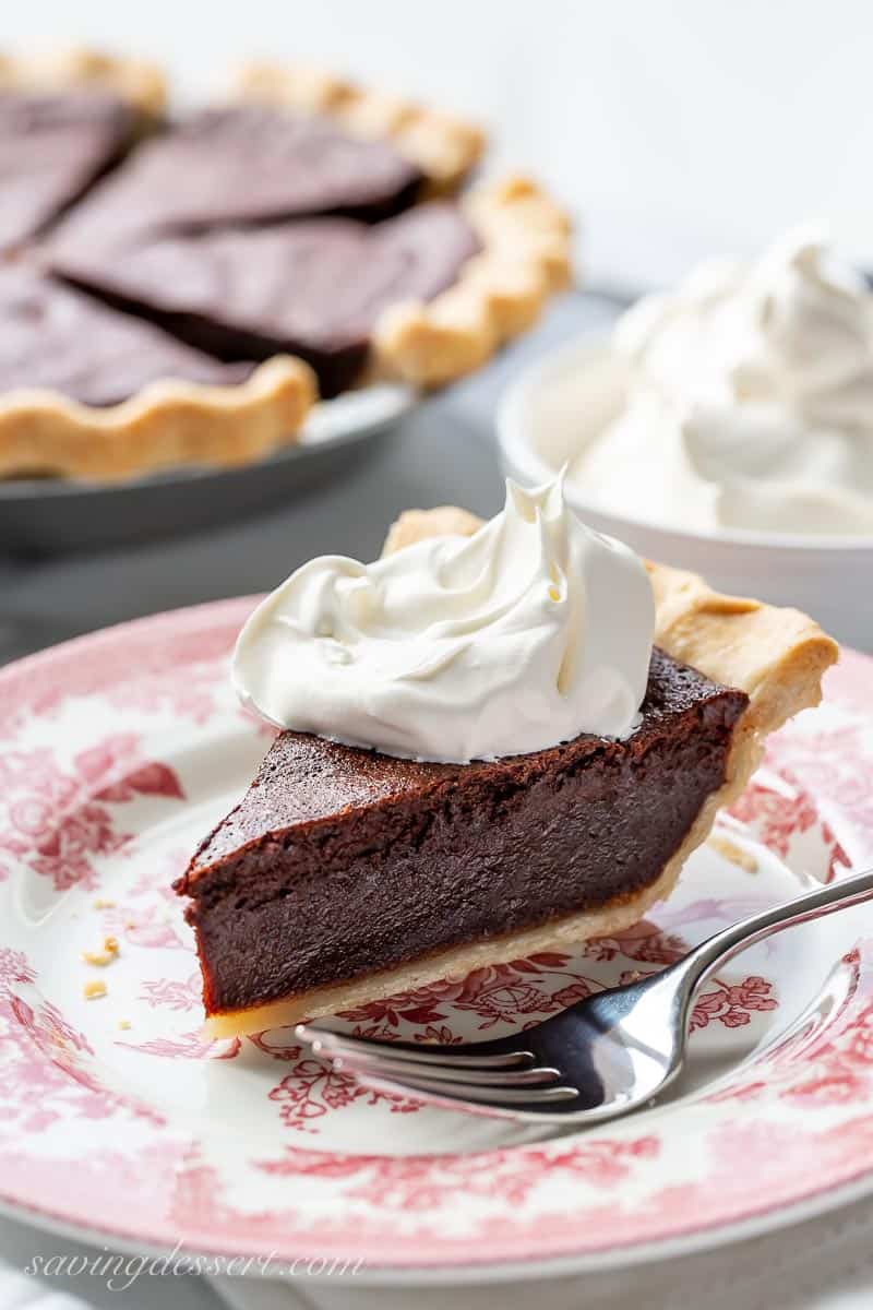 A slice of chocolate chess pie topped with a big dollop of whipped cream sitting on a plate with a fork