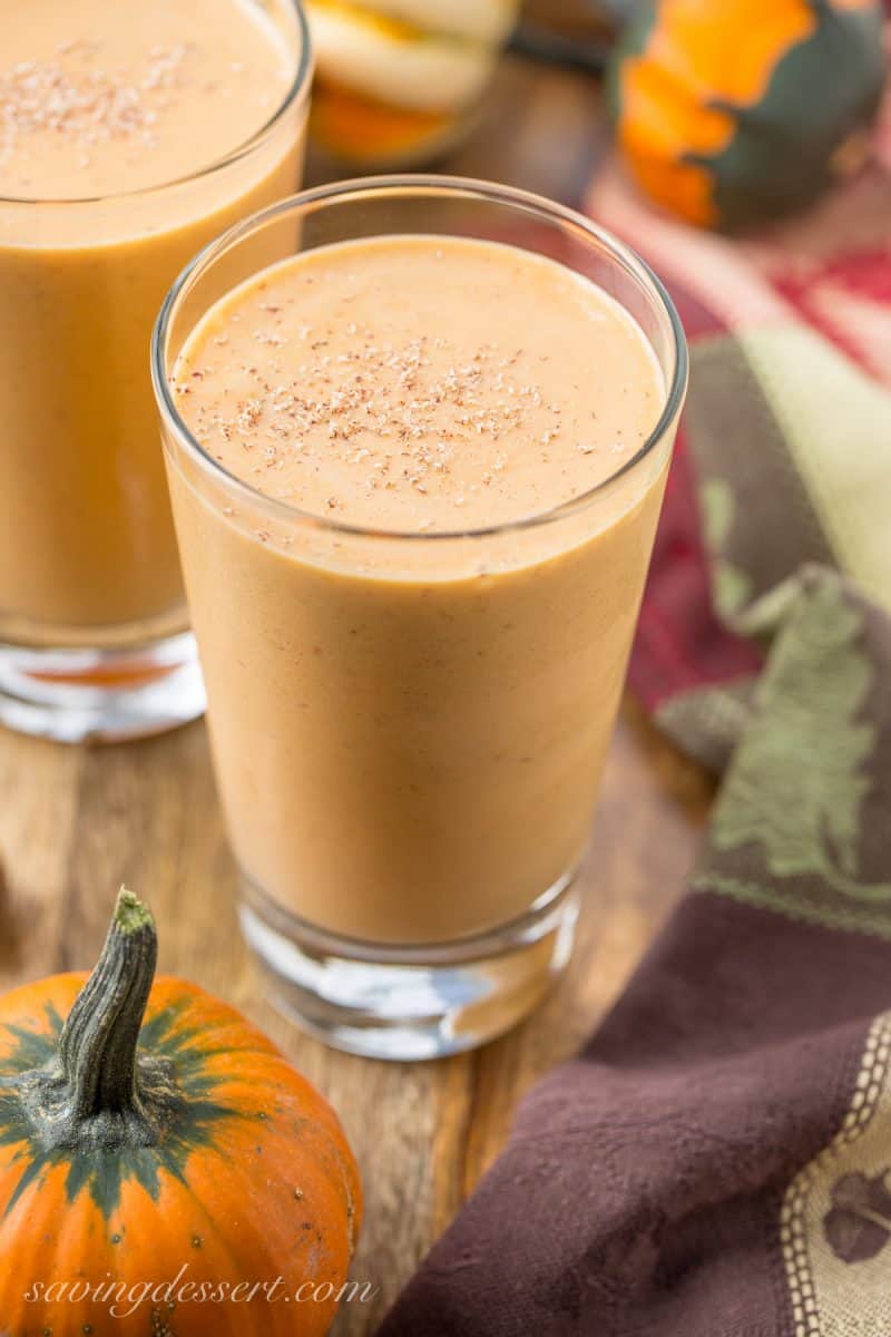 Two glasses filled with pumpkin pie smoothies with pumpkins in the background