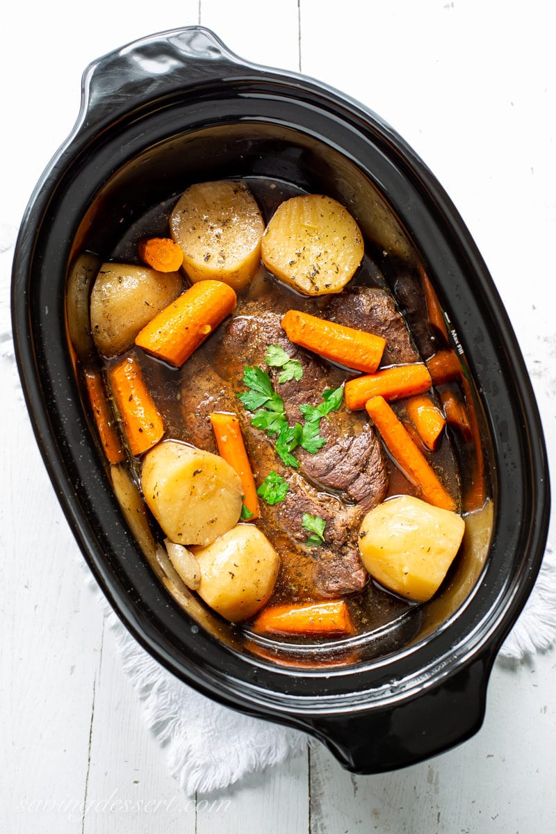 A slow cooker with a pot roast, carrots and potatoes in broth