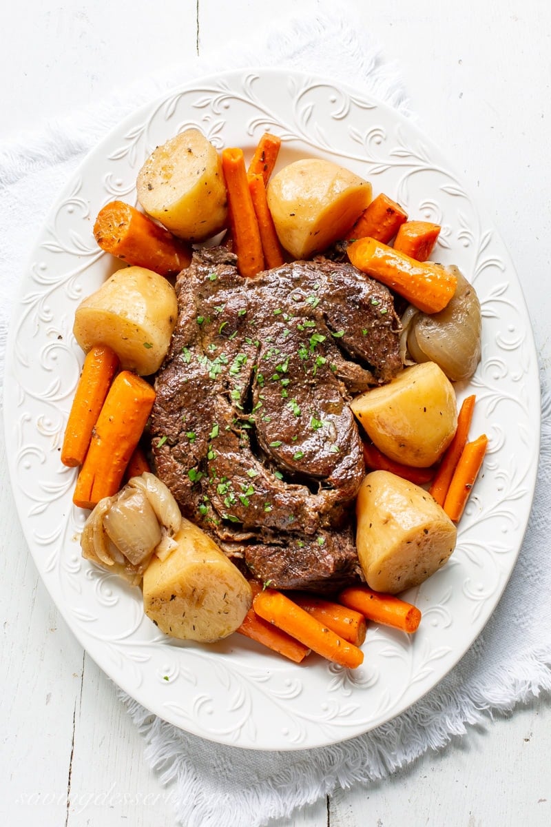 A platter with a slow cooker pot roast, potatoes, onions and carrots garnished with parsley