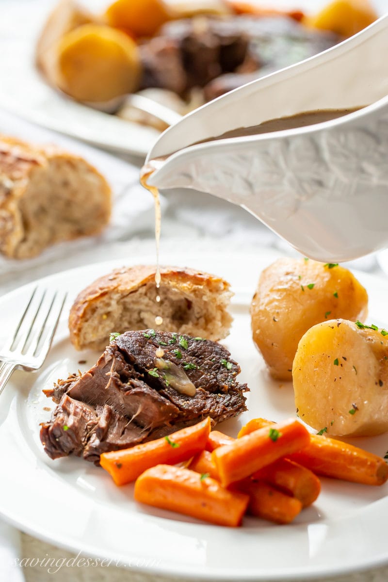 A plate of slow cooker pot roast with carrots, bread and potatoes drizzled with gravy