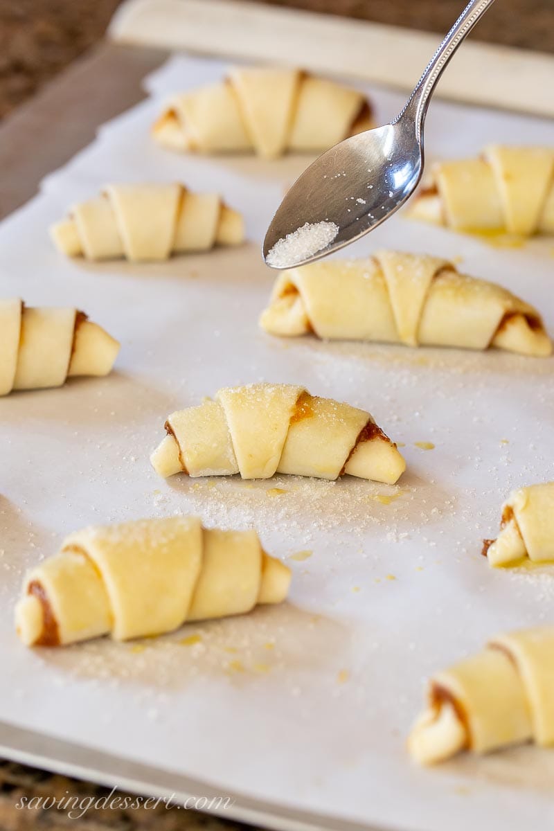 Unbaked rugelach cookies on a parchment lined baking sheet sprinkled with coarse sugar