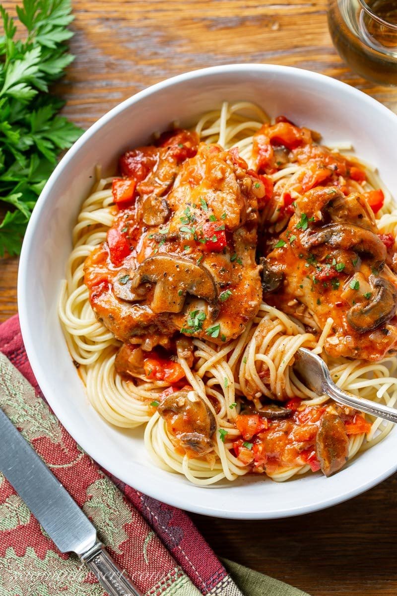 A bowl of spaghetti topped with saucy Chicken Cacciatore with red peppers, mushrooms and parsley