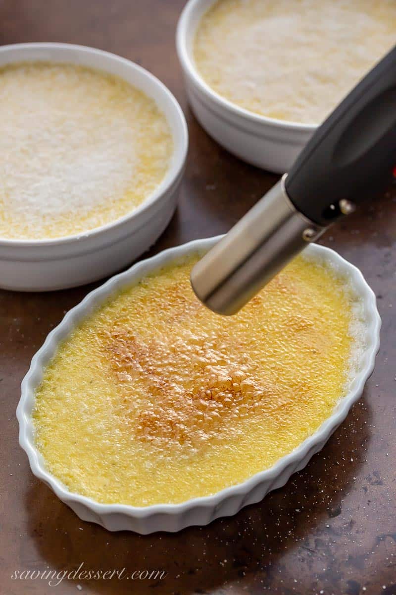 A bowl of Crème Brûlée being browned with a kitchen torch