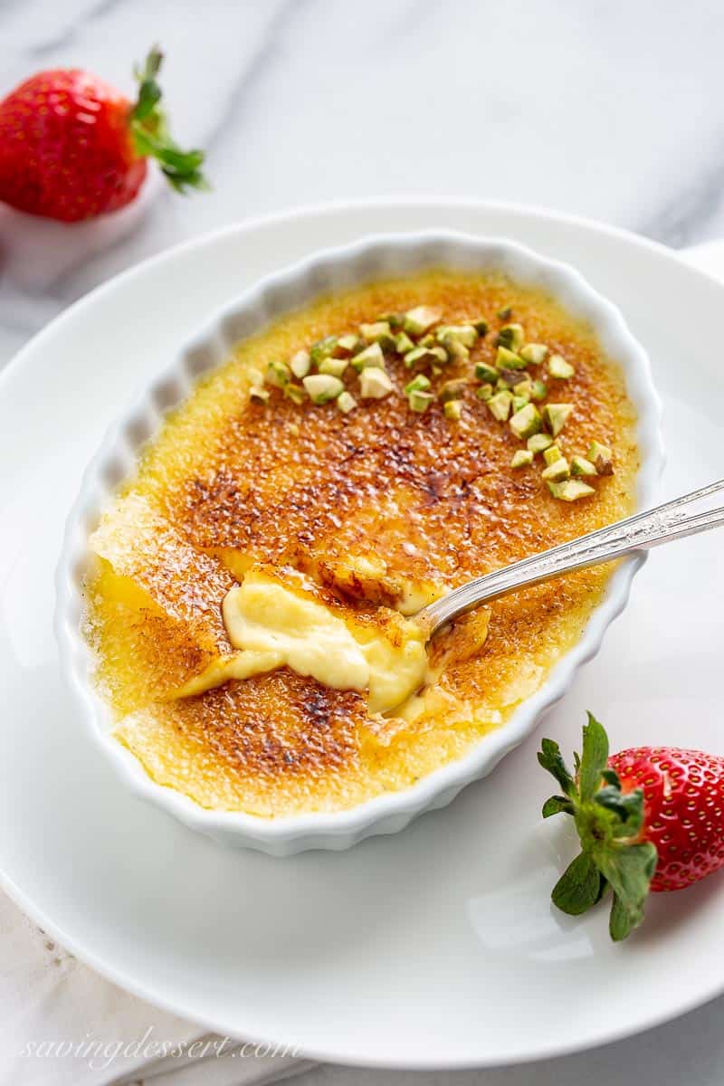 An oval dish topped with a hard candy sugar coating with chopped pistachios and fresh strawberries