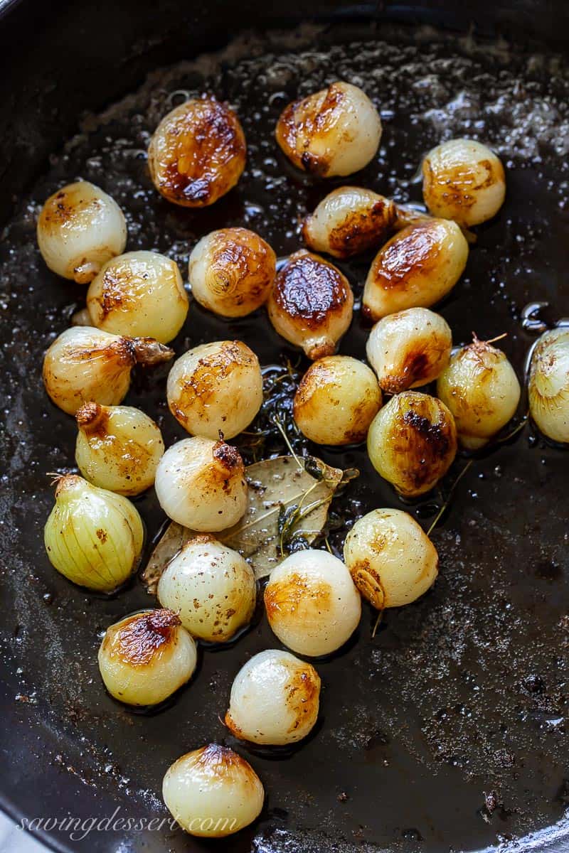 A cast iron skillet with golden brown pearl onions with herbs