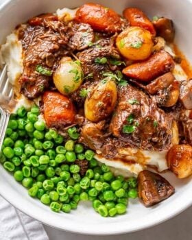 A bowl of stew served over mashed potatoes and served with peas