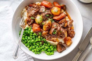 A bowl of stew served over mashed potatoes and served with peas