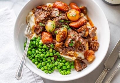 A bowl of stew served over mashed potatoes and served with peas