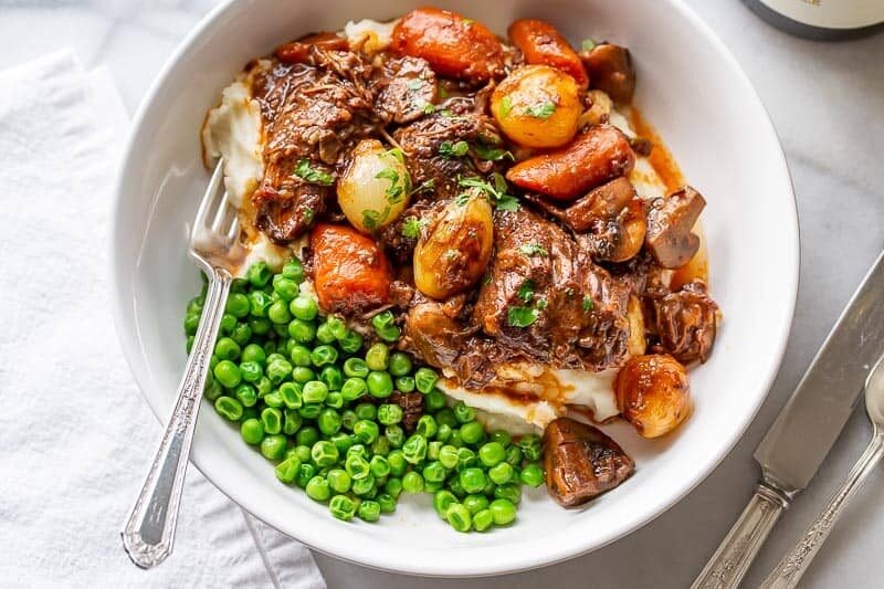 A bowl of stew served over mashed potatoes and served with peas