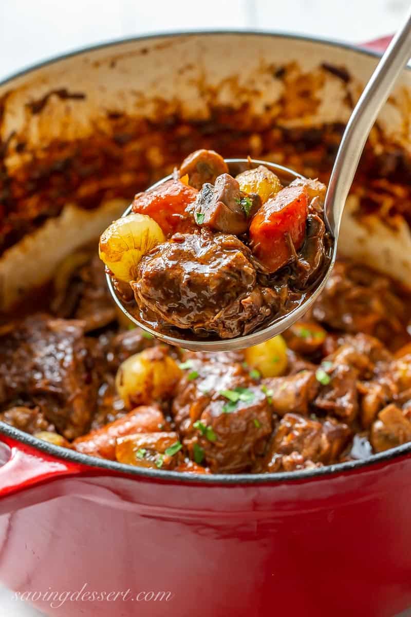 A ladle filled with Julia Child's Beef Bourguignon with carrots, onions and large chunks of beef