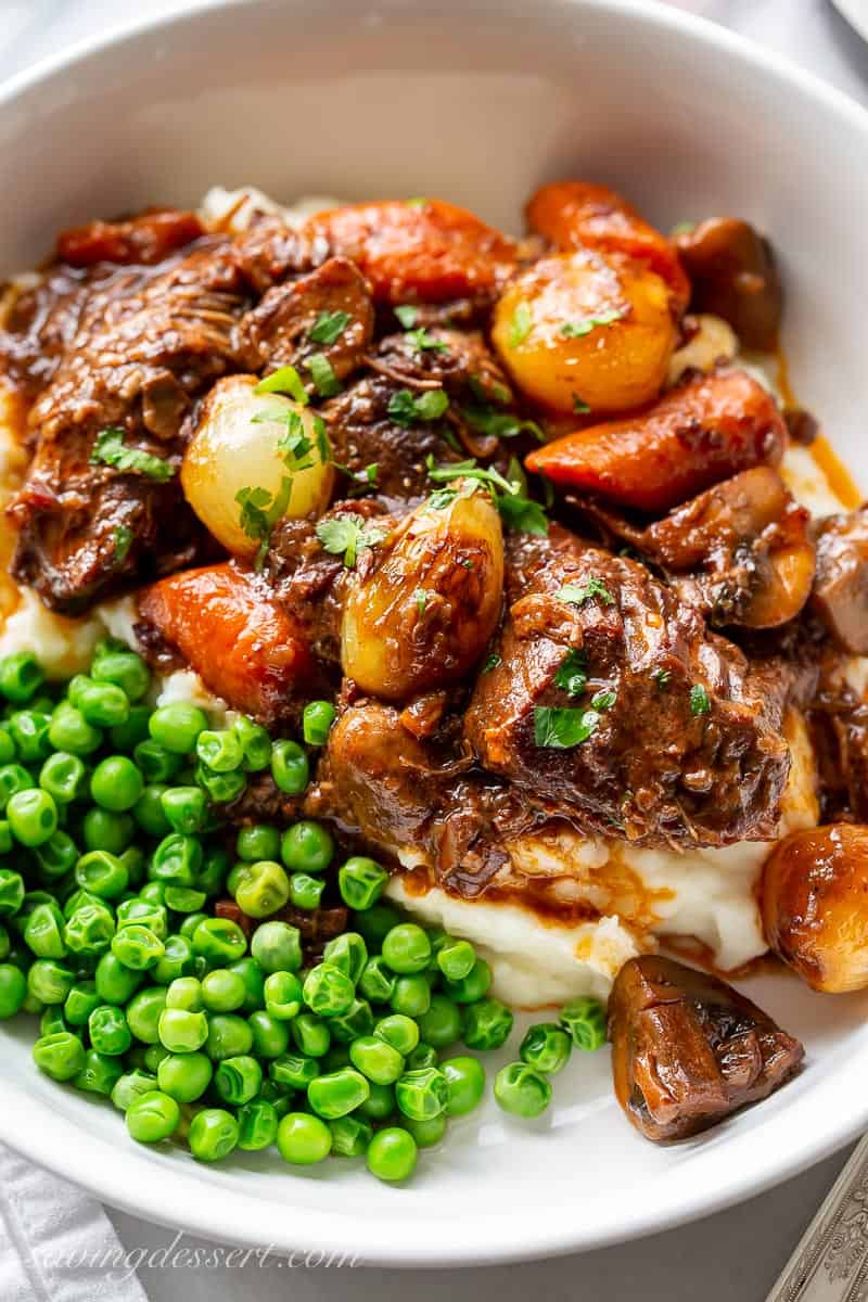An overhead view of a bowl of Julia Child's Beef Bourguignon served over mashed potatoes with peas