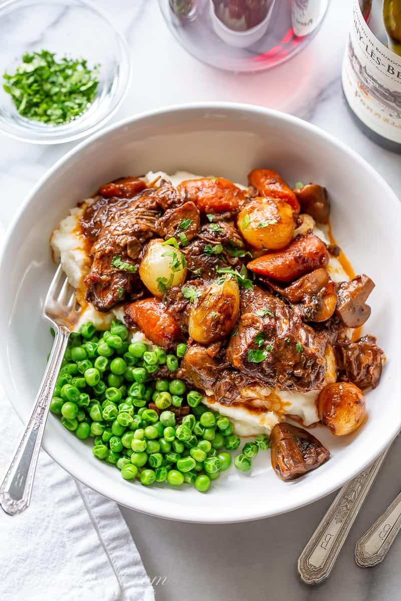 Julia Child's Beef Bourguignon in a bowl over mashed potatoes with peas