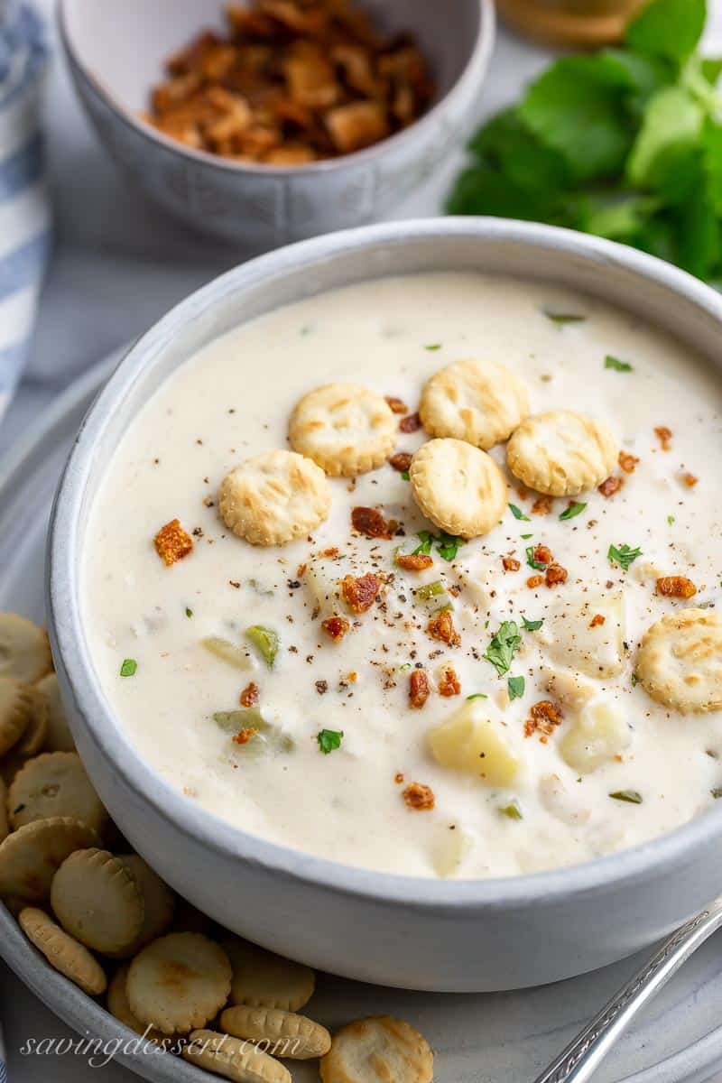 Side view of a bowl of creamy New England Clam Chowder garnished with bacon and parsley served with oyster crackers