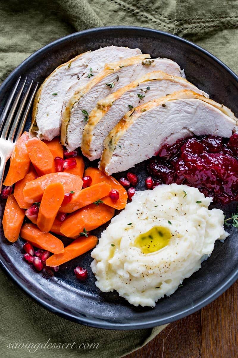 A plate of turkey, cranberry sauce, mashed potatoes and carrots garnished with a few pomegranate seeds