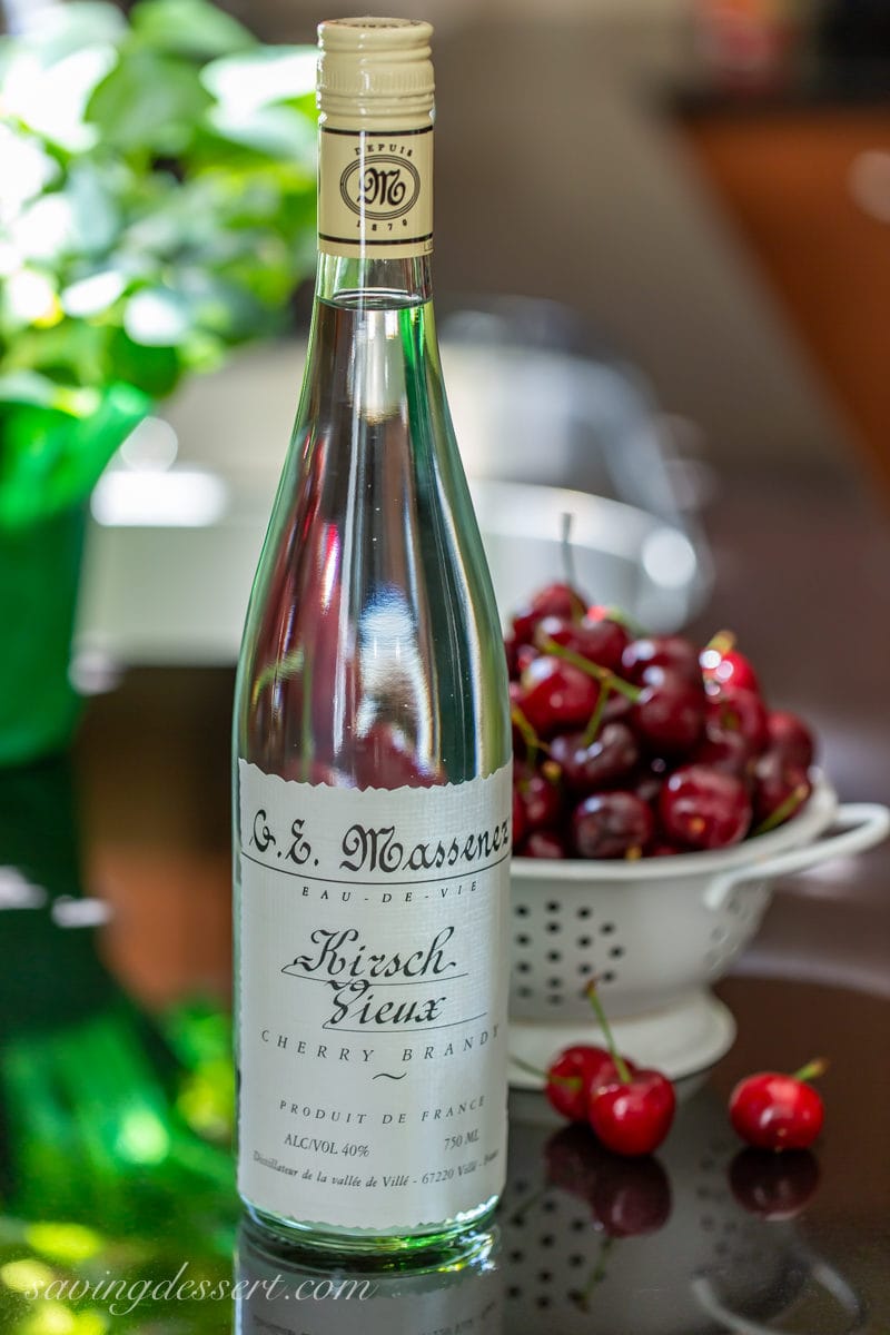 A bottle of kirsch on a kitchen countertop with fresh cherries