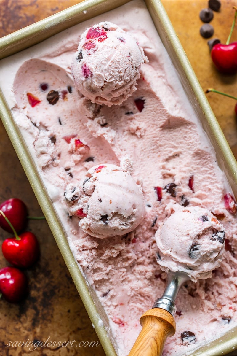 A pan of cherry ice cream with dark chocolate chunks and an ice cream scoop