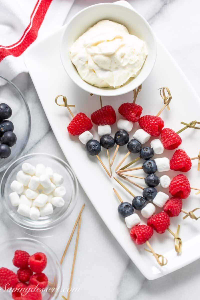 Patriotic fruit kabobs on a platter with fruit dip on the side.