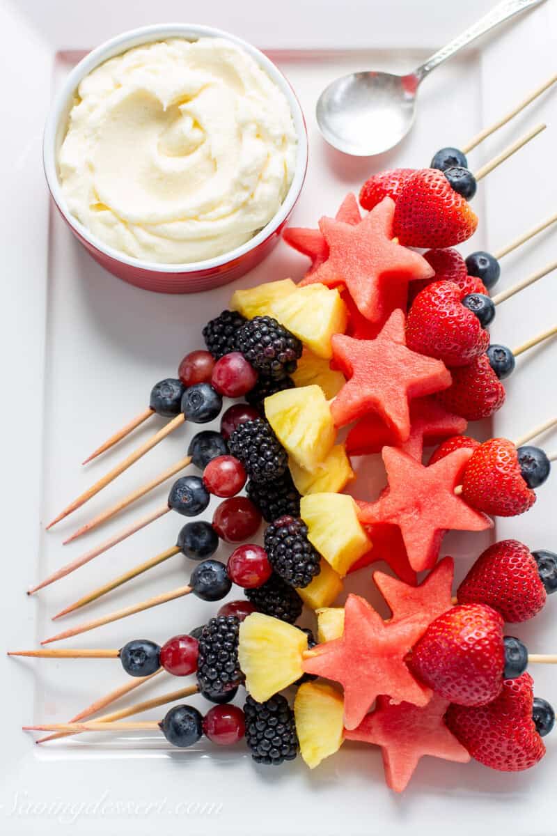 Fruit kabobs on a platter with fruit dip on the side.
