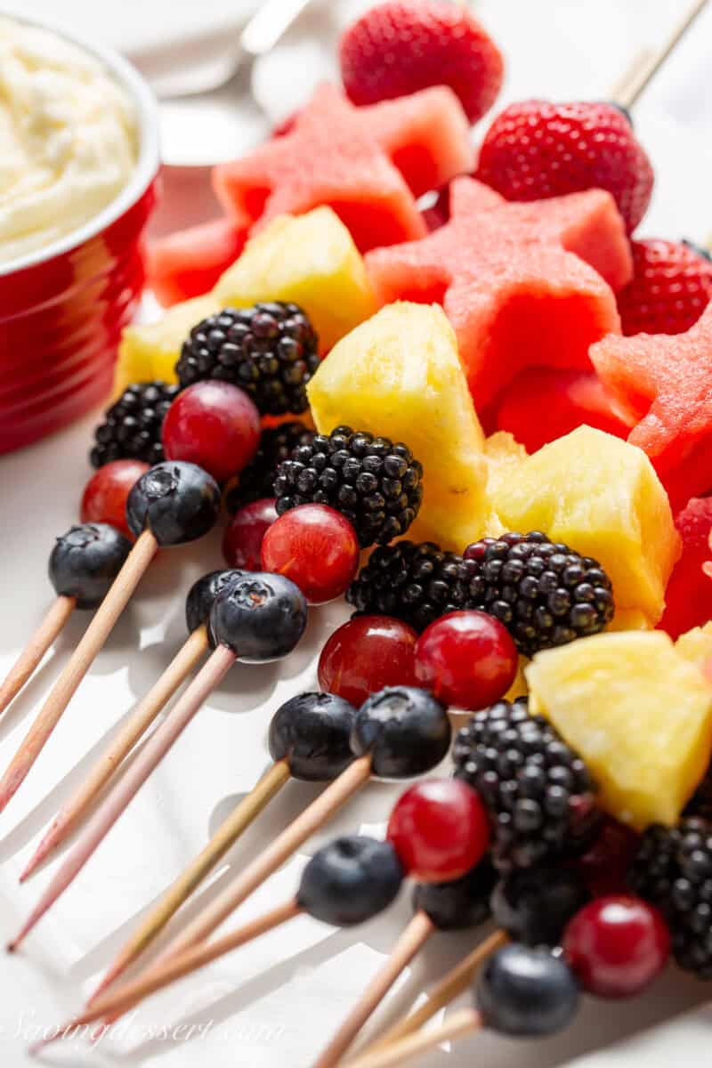 A platter filled with fruit kabobs with pineapple, grapes, blueberries, blackberries, watermelon and strawberries.