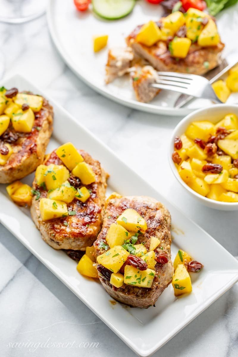 Grilled pork chops on a platter topped with an Italian peach Agrodolce sauce with raisins