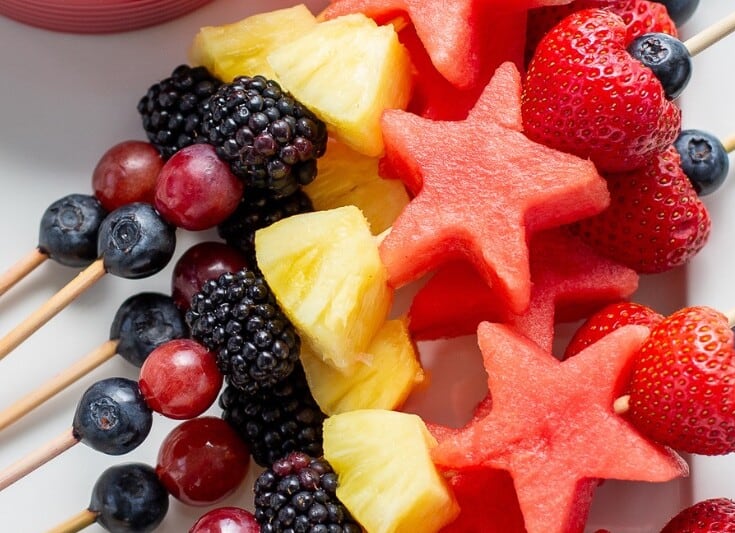 Fruit kabobs on skewers stacked on a platter.