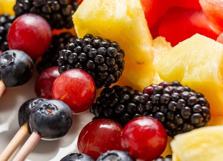 A closeup of fruit kabobs stacked on a platter.