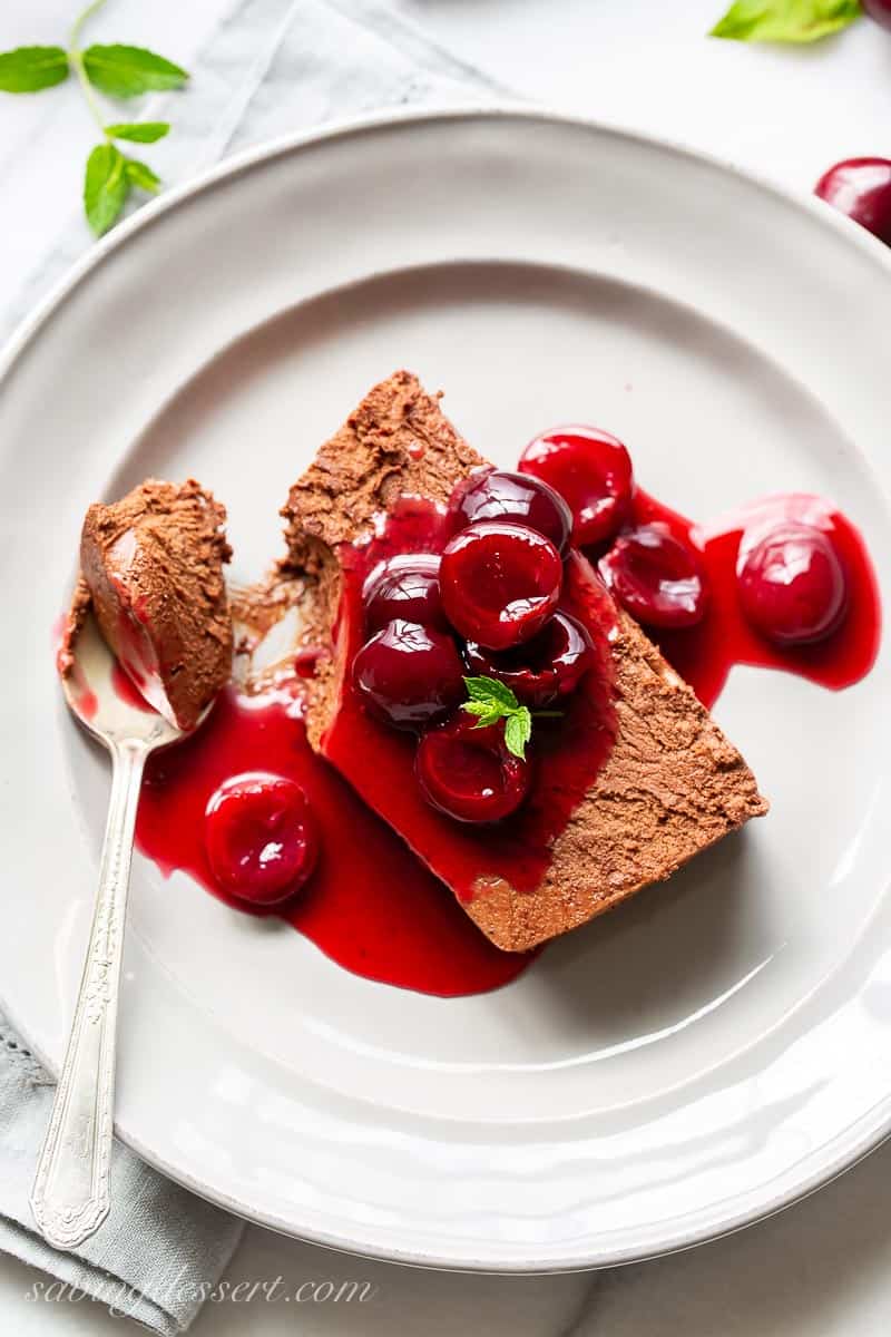 Overhead view of a slice of chocolate marquise topped with fresh cherry sauce and garnished with a sprig of mint