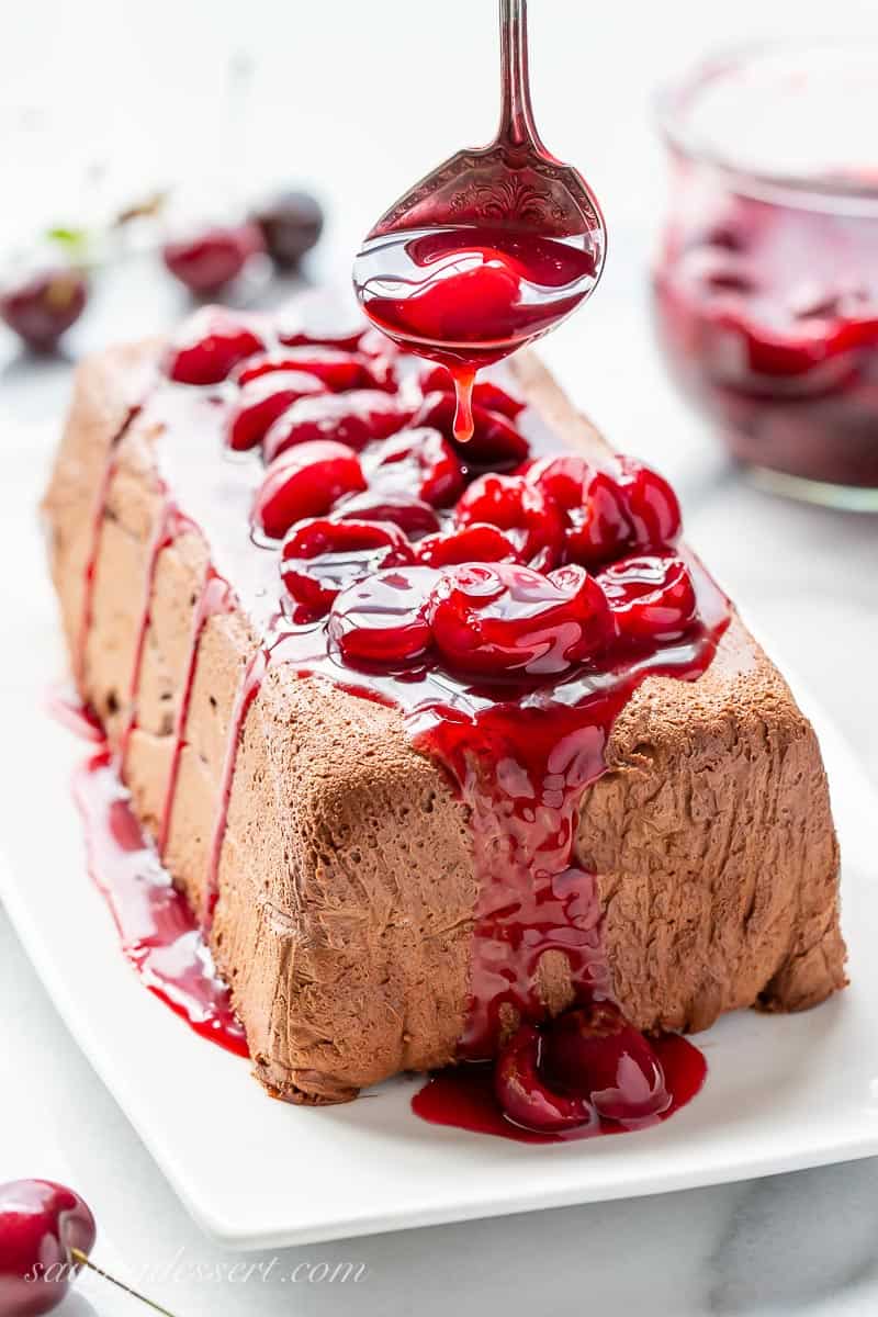 A molded chocolate marquise being drizzled with a fresh cherry sauce