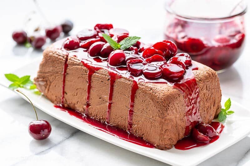 A side view of a molded Chocolate Marquise topped with fresh cherry sauce