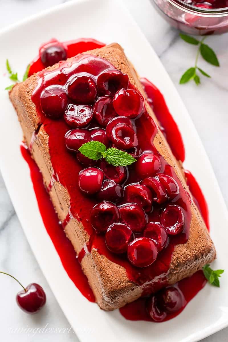 Overhead view of a chocolate marquise on a platter with fresh cherry sauce spooned on top