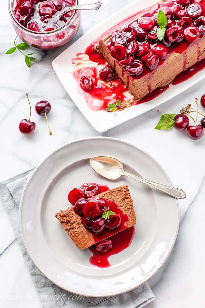 Chocolate Marquise on a plate, a jar of fresh cherry sauce and an unfolded loaf of chocolate semifreddo