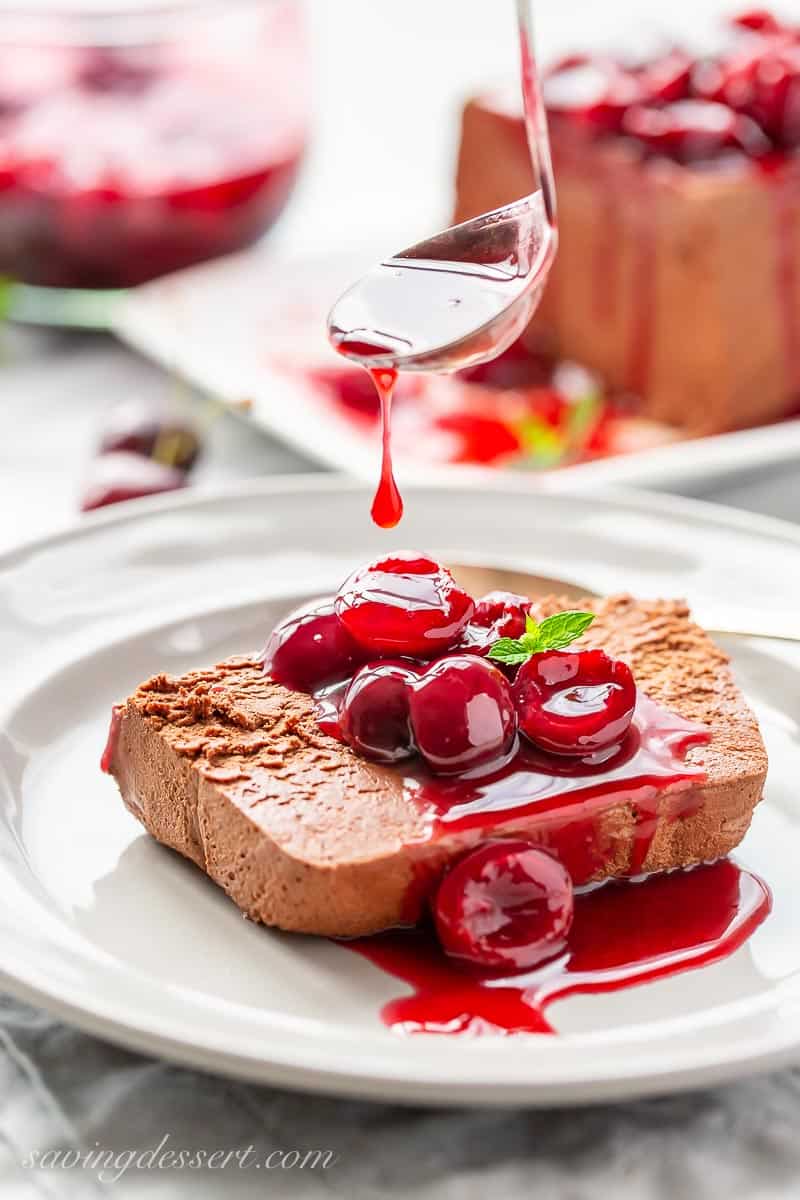 A slice of chocolate marquise on a plate being drizzled with fresh cherry sauce
