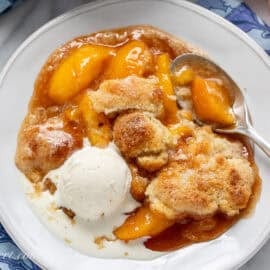 A bowl of peach cobbler with a scoop of vanilla ice cream on top.