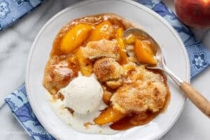 A bowl of peach cobbler with a scoop of vanilla ice cream on top.