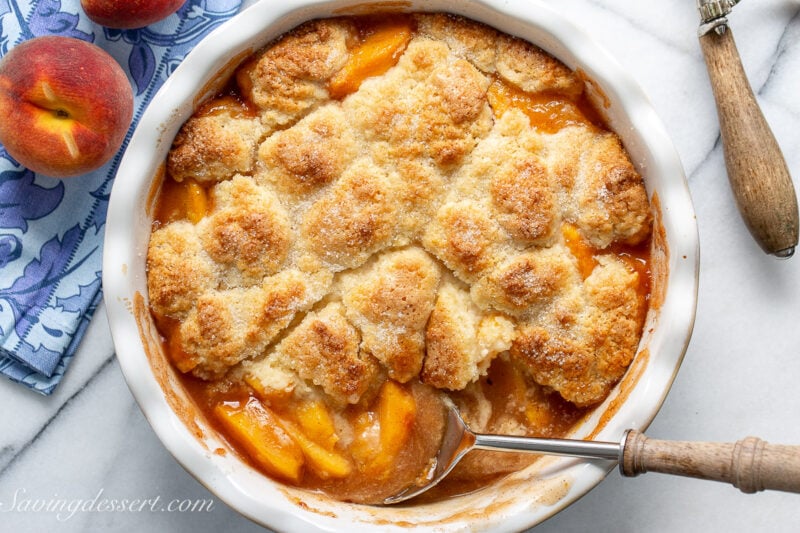 A deep dish pie plate filled with warm peach cobbler with a biscuit topping.