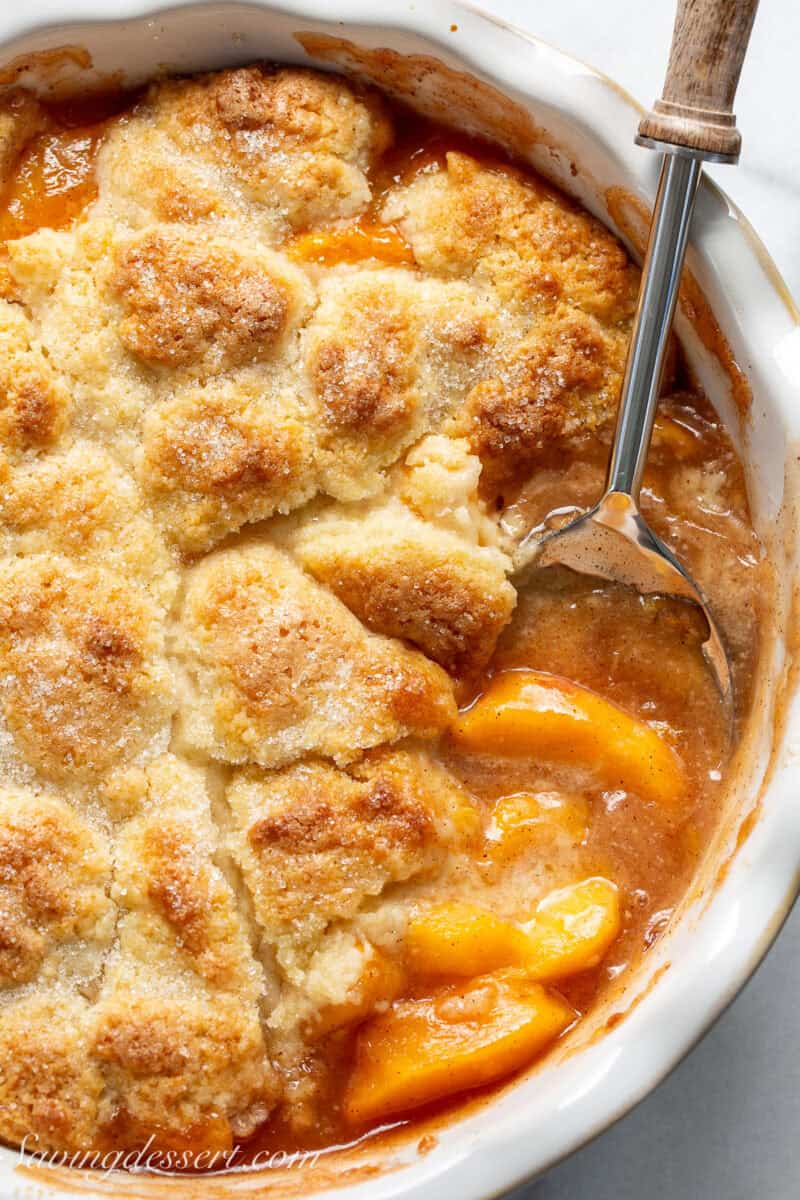 A pan of peach cobbler with a spoon scooping out a serving.