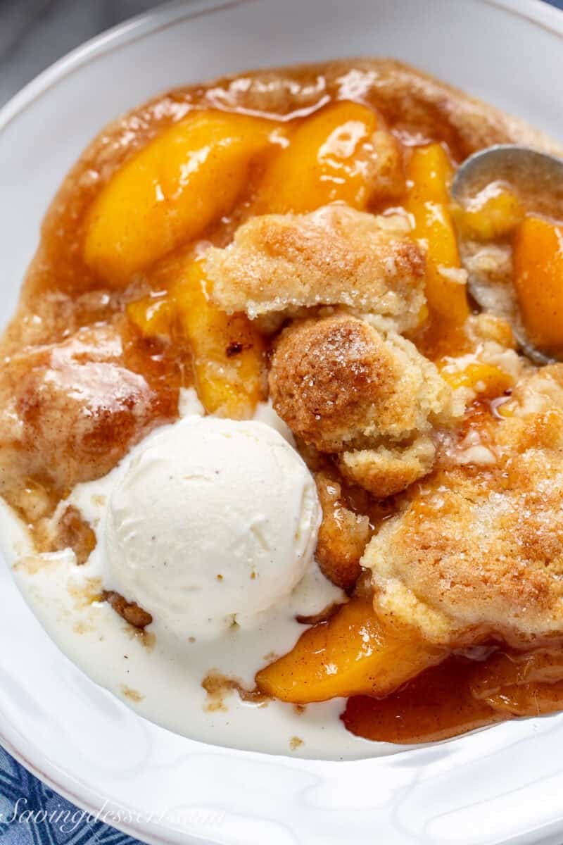 A closeup of a bowl of peach cobbler with ice cream on top.