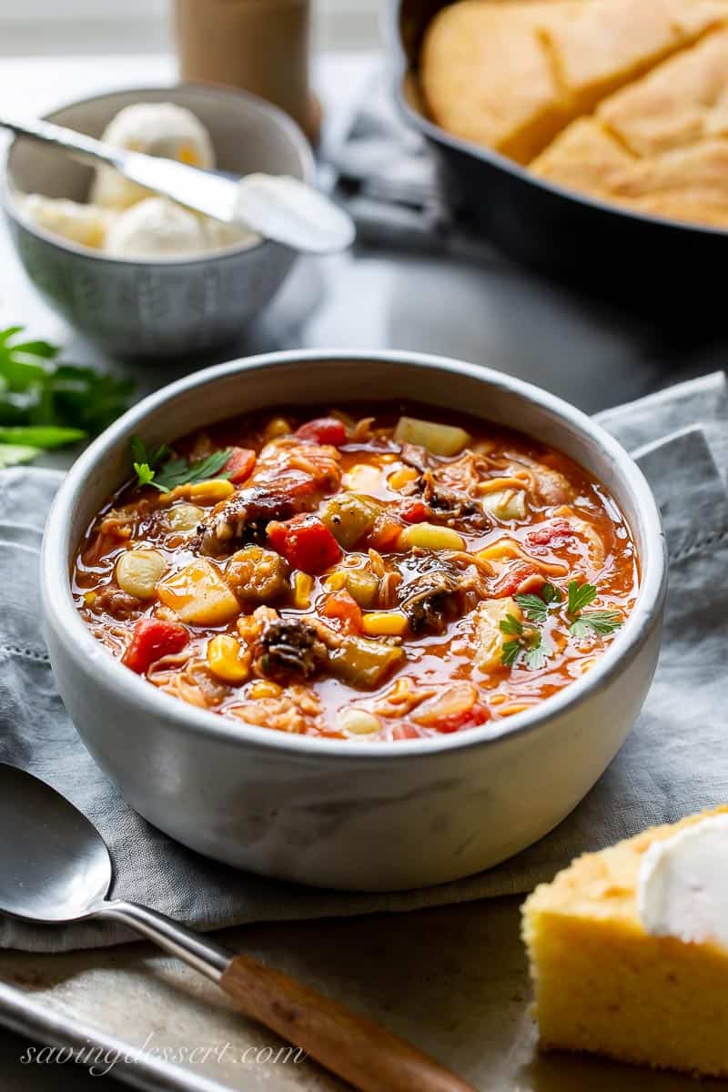 A side view of a bowl of Brunswick Stew served with cornbread and butter