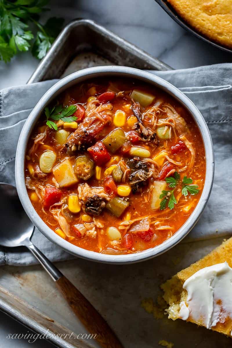 A bowl of tomato based Brunswick Stew on a small baking tray served with buttered cornbread