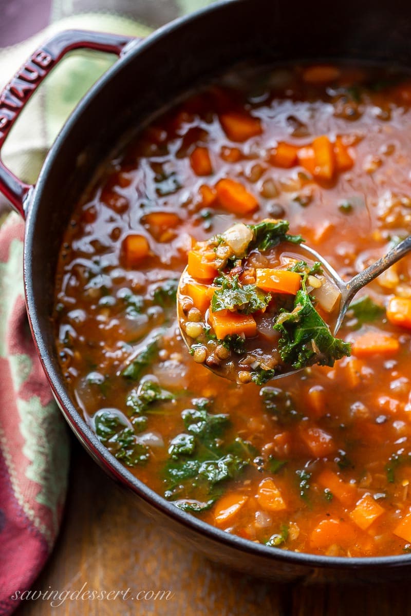 A ladle filled with carrots, kale and lentil soup