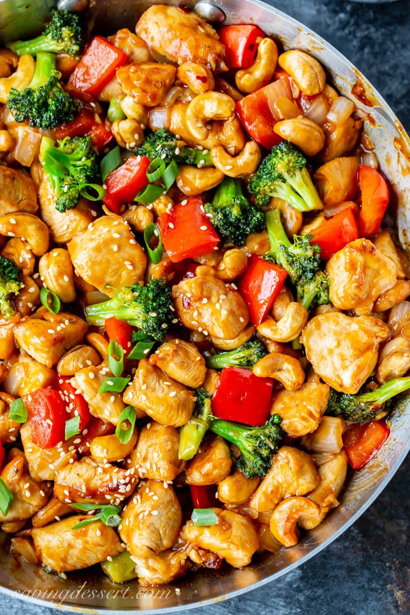 Overhead view of a skillet with Honey Cashew Chicken. Loaded with cashews, red bell pepper, broccoli, onions and garnished with green onions and sesame seeds