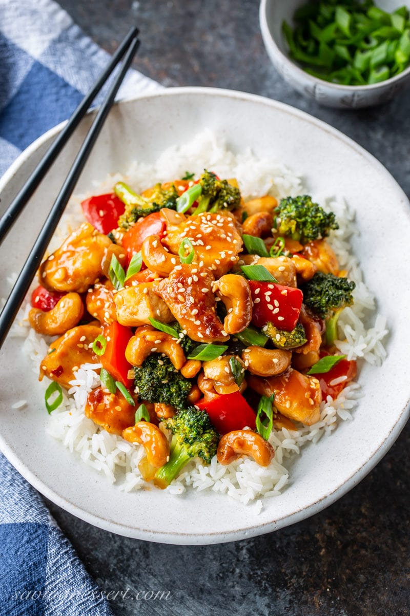 A bowl of Jasmine rice topped with Honey Cashew Chicken with red bell pepper, broccoli, onions and cashews. Garnished with sesame seeds and sliced green onions.