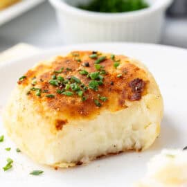 A closeup photo of a partially eaten mashed potato cake topped with chopped chives.
