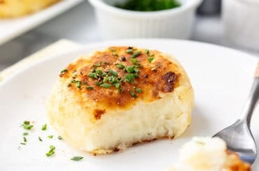 A closeup photo of a partially eaten mashed potato cake topped with chopped chives.