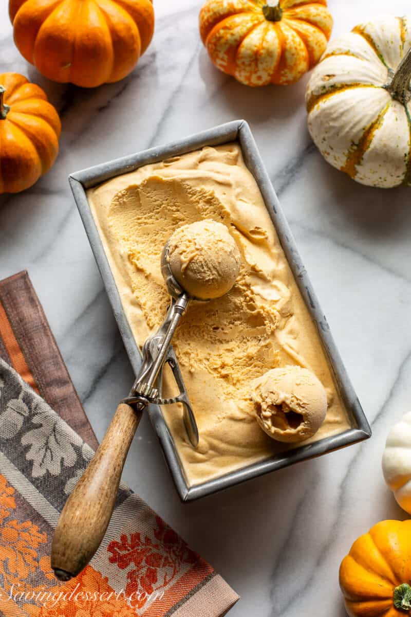 An overhead view of a pan filled with pumpkin ice cream with an ice cream scoop on top.