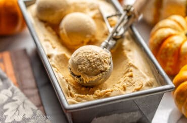 A loaf pan filled with pumpkin ice cream with scoops and an ice cream scooper on top.