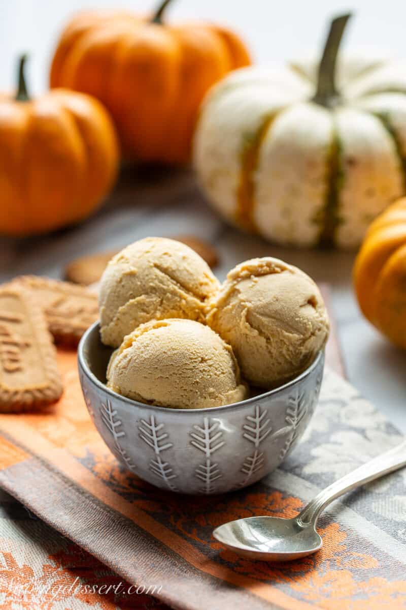Scoops of pumpkin ice cream in a bowl with mini pumpkins in the background.