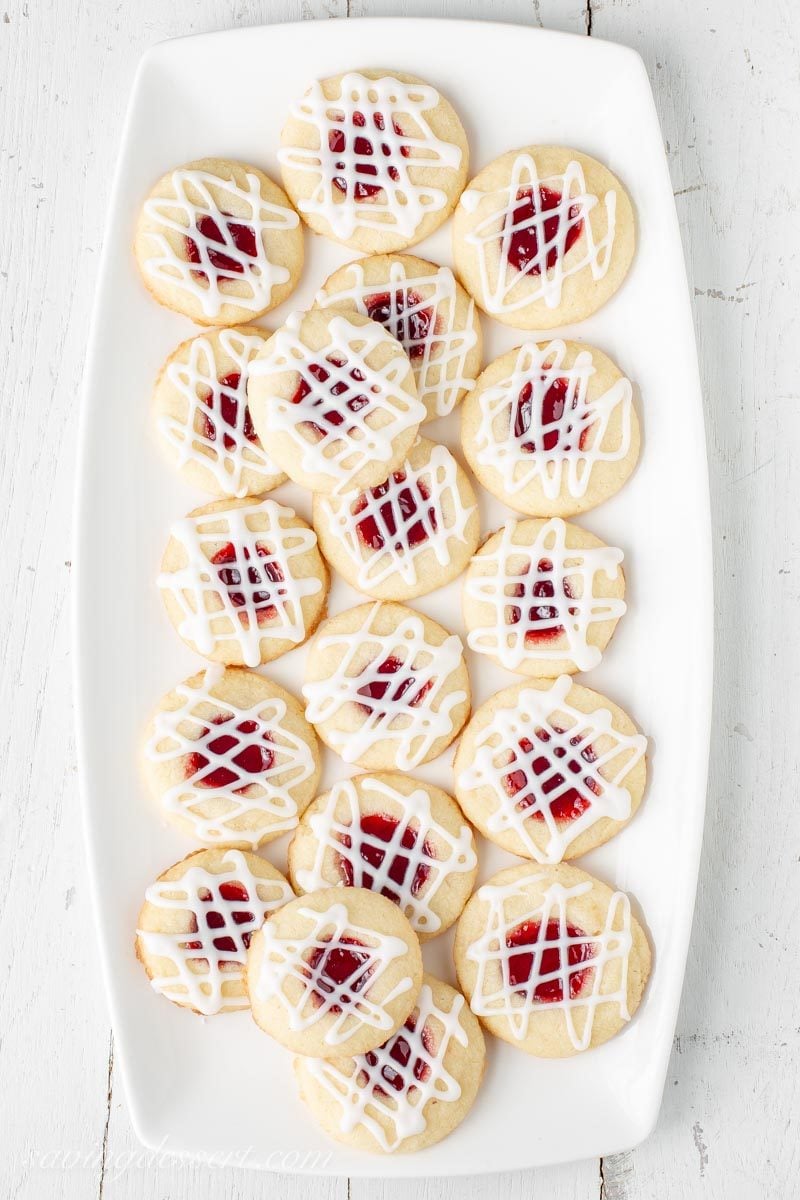 A plate of raspberry almond shortbread thumbprint cookies with a drizzled almond icing